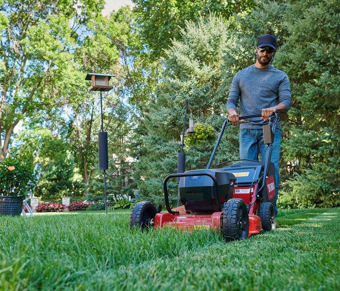 Routine Yard Maintenance with Mower Man trimming the grass with a gas lawn mower.