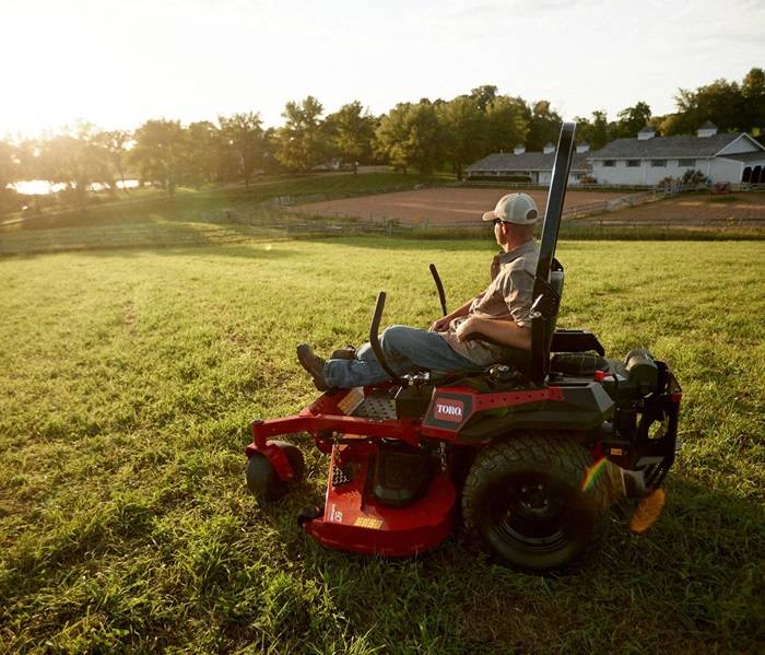 Handling Lawn Care with a Powerful Riding Mower Homeowner mowing his lawn during a bright afternoon with a gas mower.